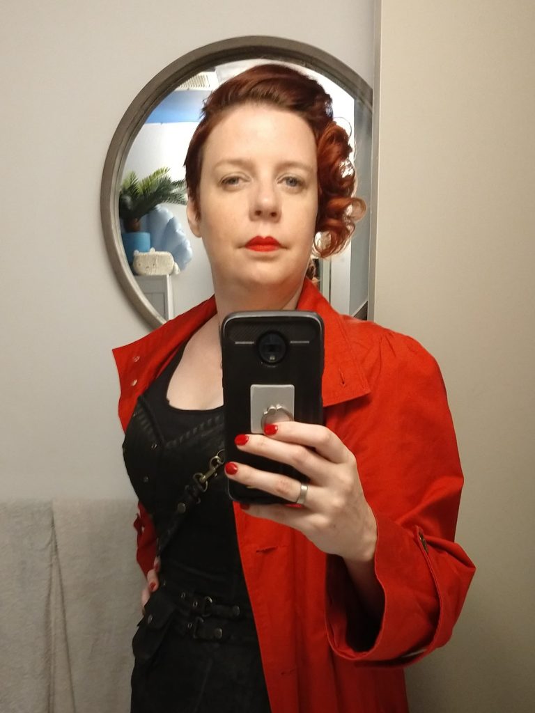 A selfie in front of the mirror by Victoria, who has curled her hair and is wearing a black corset and red coat.